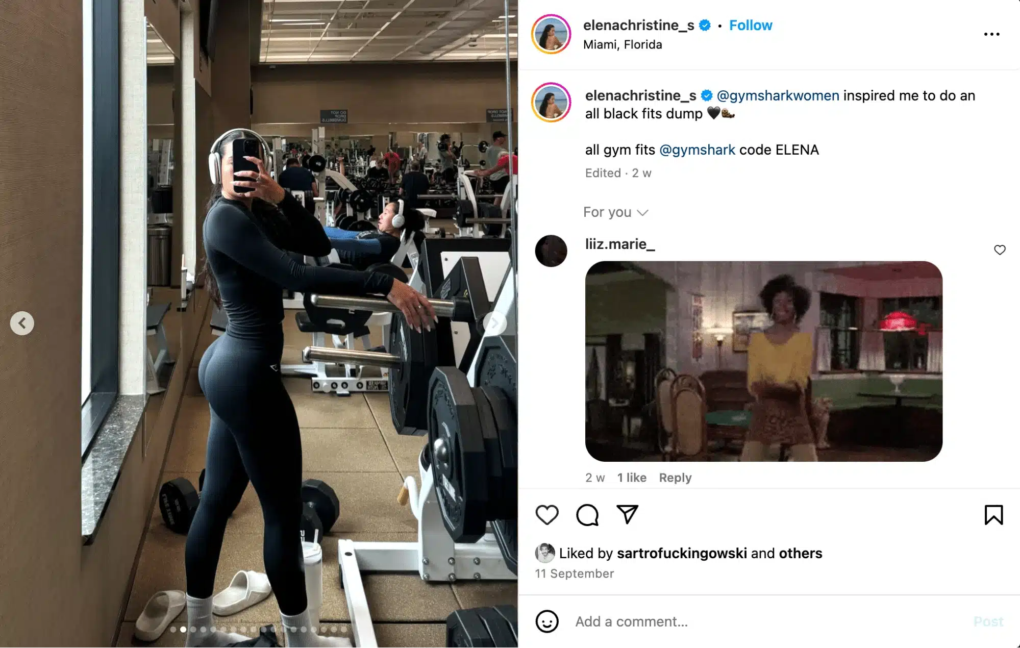 Woman taking a mirror selfie in a gym, wearing an all-black fitted workout set and headphones while leaning on a weight machine; strength equipment and other gym-goers are visible in the background, shown within an Instagram post interface with caption and engagement icons.