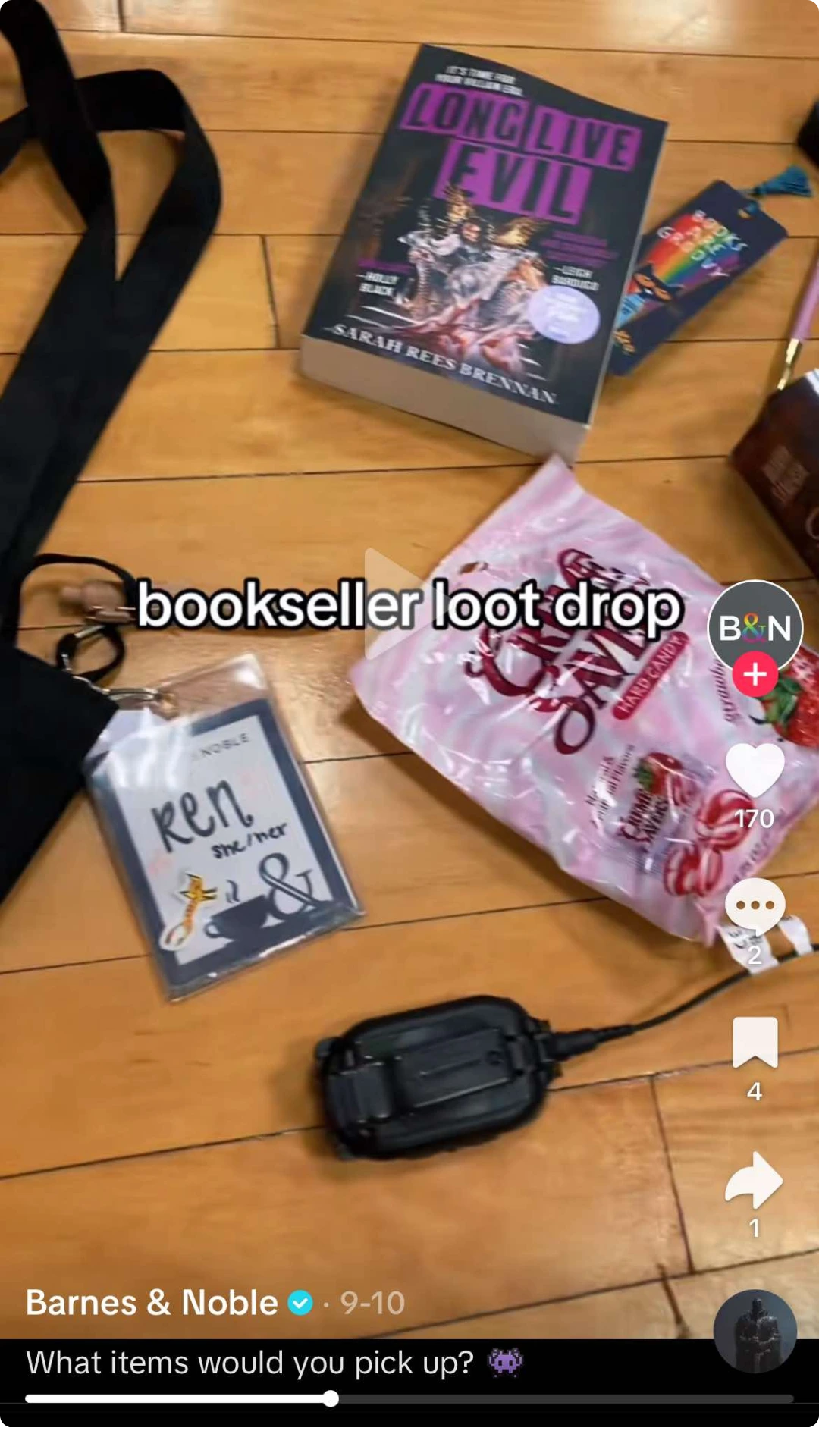 TikTok video from Barnes & Noble showing a bookseller haul spread on a wooden floor, including a copy of Long Live Evil by Sarah Rees Brennan, candy, bookmarks, and a staff name badge. On-screen text reads “bookseller loot drop,” and the TikTok interface displays engagement metrics and a caption asking viewers which items they would pick up.