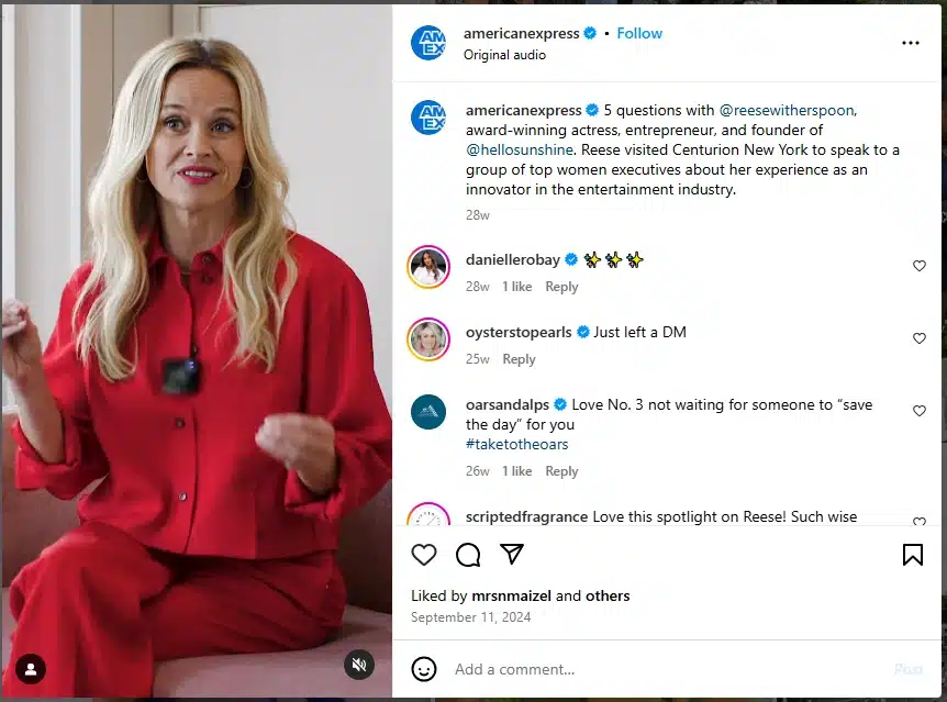 Reese Witherspoon sits in a red outfit against a minimalist background, mid-speech, in a video post by American Express highlighting her talk at Centurion New York about innovation and leadership.