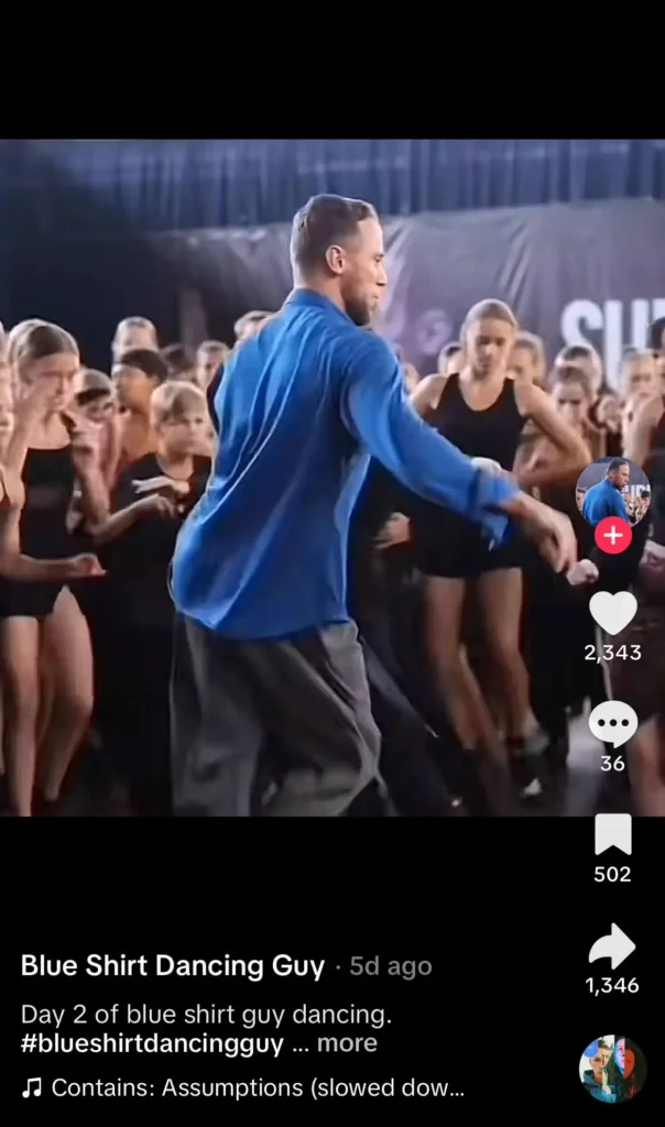 Man in a blue shirt dancing energetically in front of a cheering crowd.