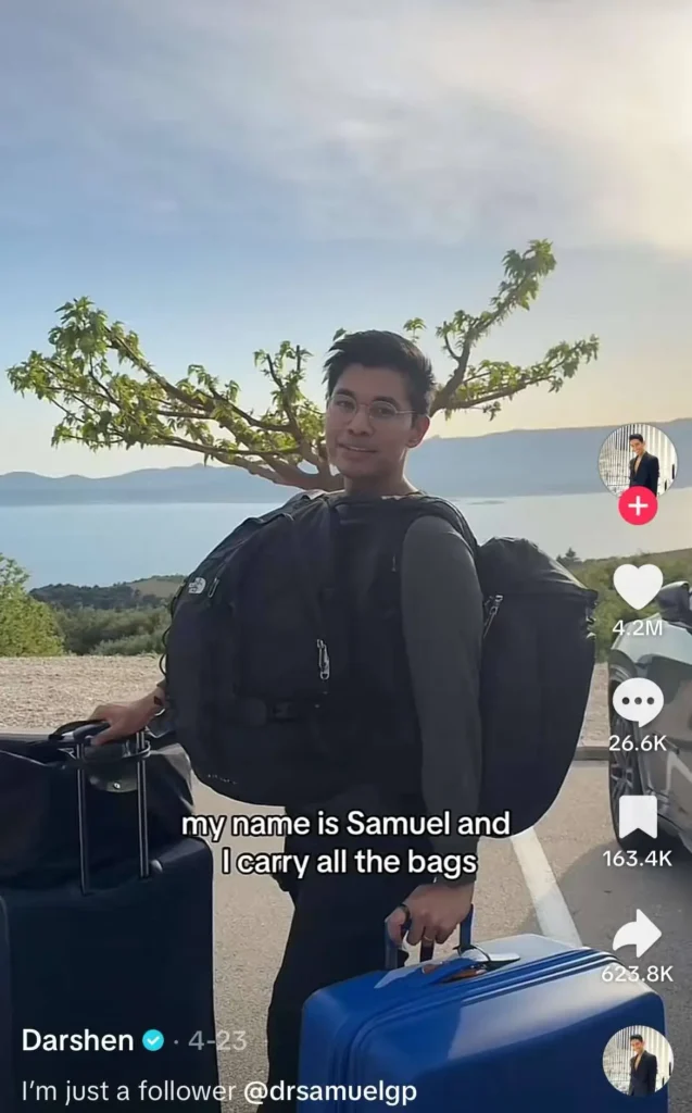A person standing on a road with a scenic background of trees, water, and mountains, carrying multiple bags. Text overlay reads: "my name is Samuel and I carry all the bags."