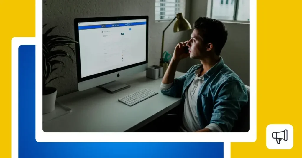 Person seated at a modern desk, thoughtfully looking at an iMac screen, with a lamp, plant, and window in the background.
