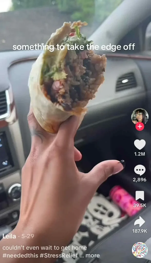 A person holding a half-eaten burrito in a car like a cigarette with the caption 'something to take the edge off.' 