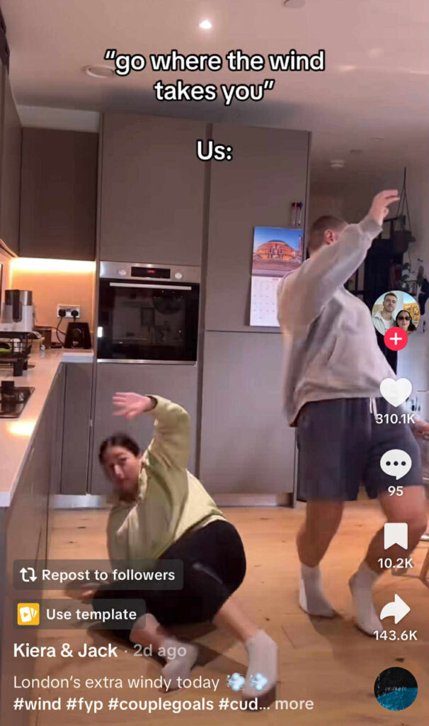 A couple in a kitchen acting out the caption ‘go where the wind takes you,’ with the woman on the floor and the man leaning back as if blown by wind.