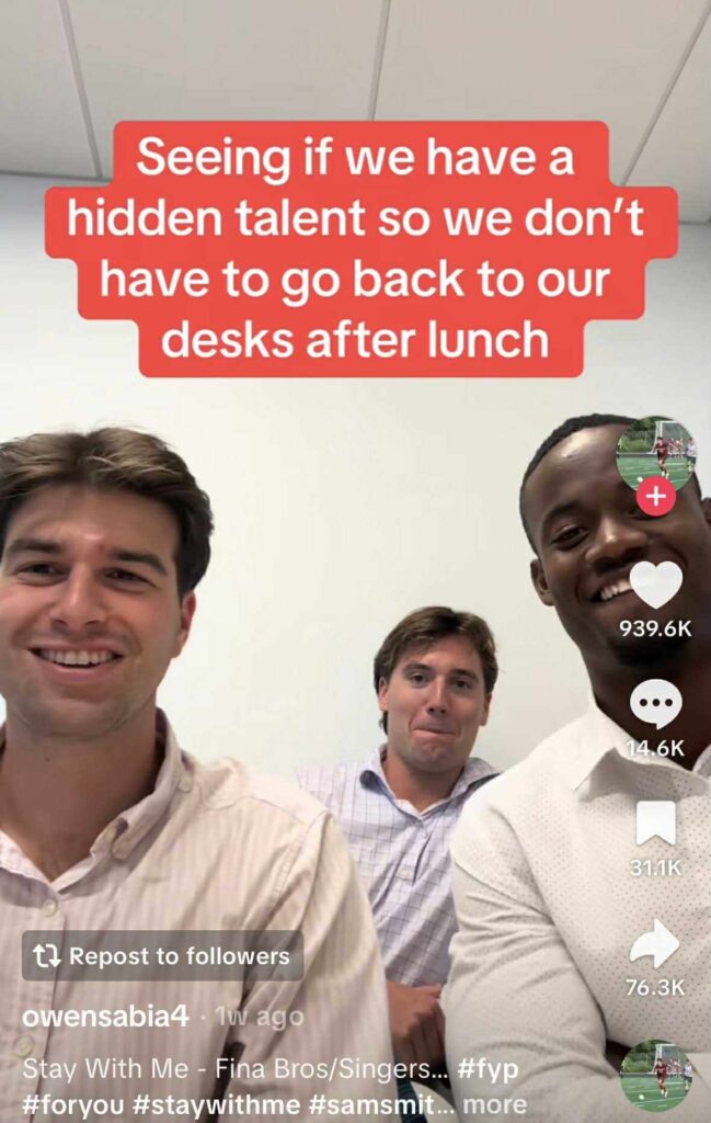 Three men sitting in an office smiling at the camera, with a red text overlay that reads, “Seeing if we have a hidden talent so we don’t have to go back to our desks after lunch.”