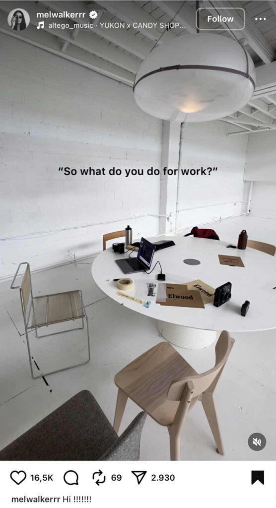 Instagram Reel showing a minimal white office setup with a round table, scattered papers labeled ‘Elwood,’ a laptop, cameras, tape, and water bottles. Overlay text reads ‘So what do you do for work?’