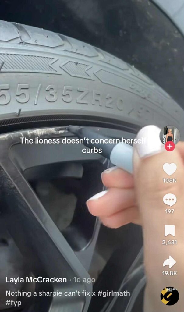 A close-up of a car tire with scratches on the rim, as a person uses a gray marker to cover up the damage.