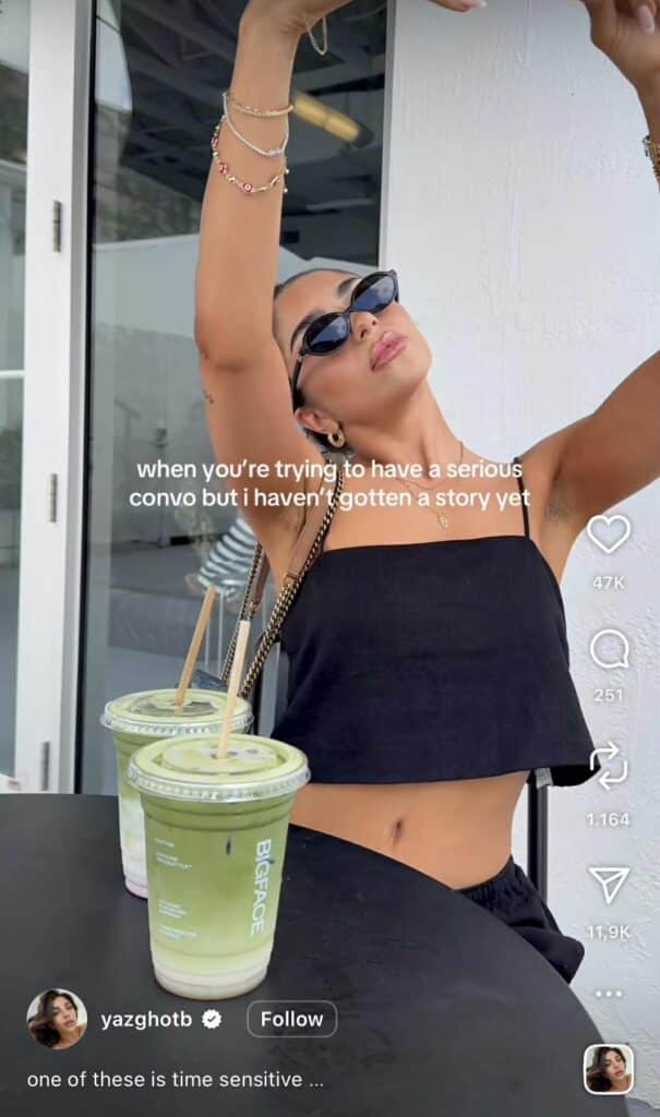 Instagram Reel of a woman in sunglasses and a black crop top posing for a selfie while holding her arm up. The on-screen caption reads, “when you’re trying to have a serious convo but i haven’t gotten a story yet.” Two iced matcha drinks sit on the table in front of her.