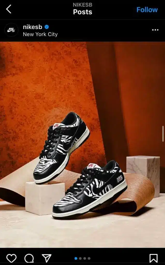 Pair of black and white Nike SB sneakers with zebra print displayed on a beige and orange studio backdrop, styled on geometric platforms in a product showcase.