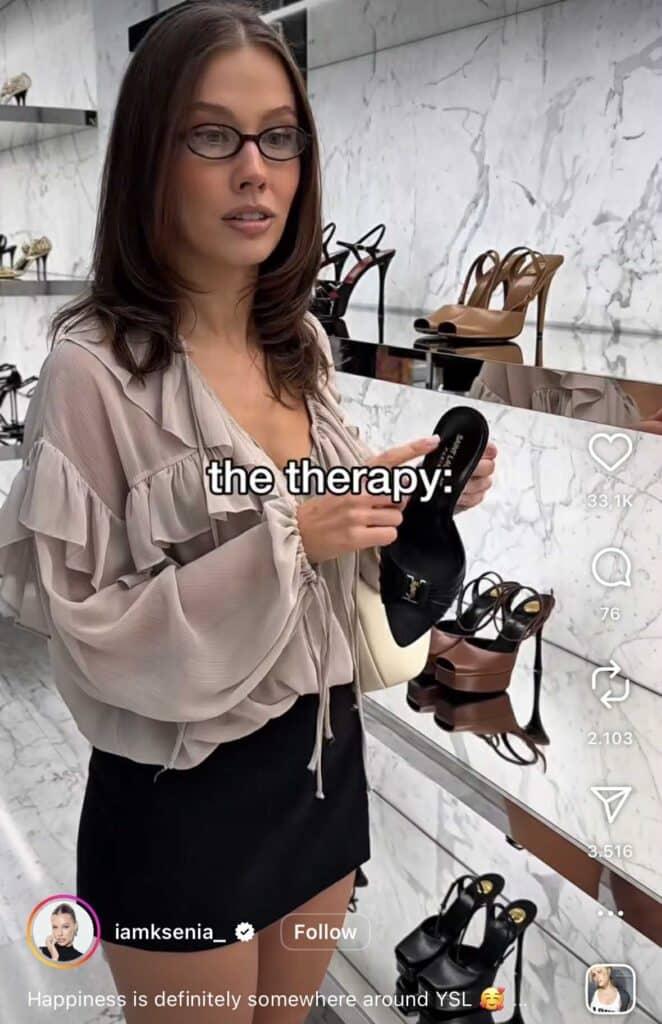Instagram Reel of a woman shopping for luxury shoes in a store, holding a black YSL heel and pointing at it. The on-screen caption reads “the therapy:”. Shelves of high heels are displayed behind her.