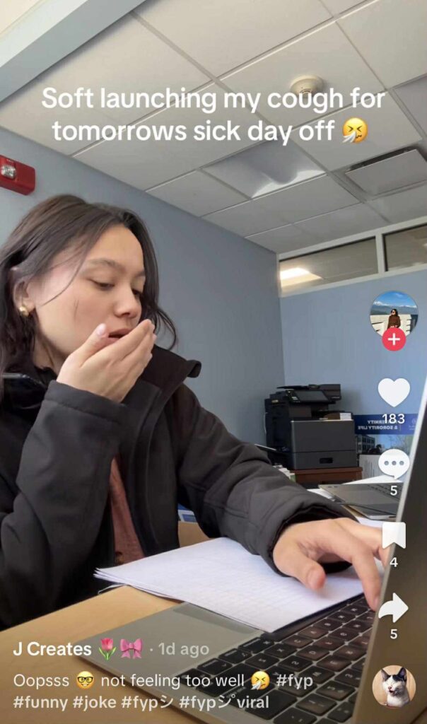 A person sitting at a desk in an office, covering their mouth as if coughing while looking at a laptop. Text on the image reads, “Soft launching my cough for tomorrow’s sick day off."