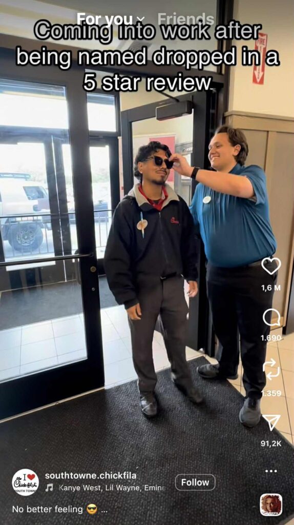 Two Chick-fil-A employees stand by the restaurant entrance smiling. One employee wears sunglasses and walks confidently while the other adjusts them, as the caption reads, “Coming into work after being name dropped in a 5 star review.”