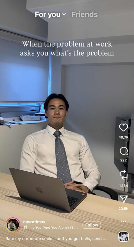 A man in a white dress shirt and patterned tie sits at an office desk with a laptop in front of him, staring straight ahead with a blank, slightly tense expression. The caption above him reads, “When the problem at work asks you what’s the problem.”