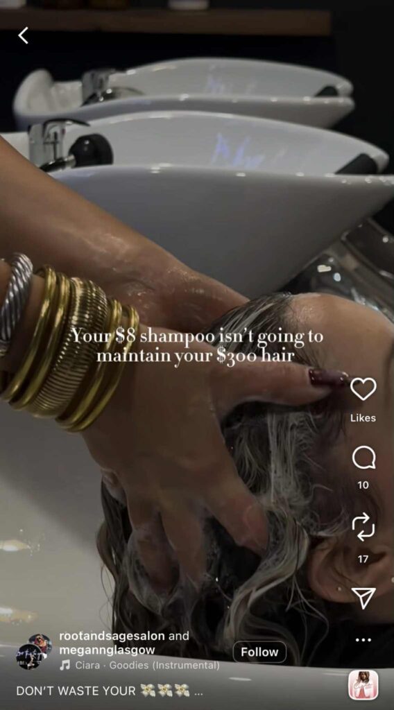 A close-up shot of a hairstylist washing a client’s hair at a salon sink, with the stylist’s hands massaging shampoo into the client’s scalp. White text on the screen reads, “Your $8 shampoo isn’t going to maintain your $300 hair.”
