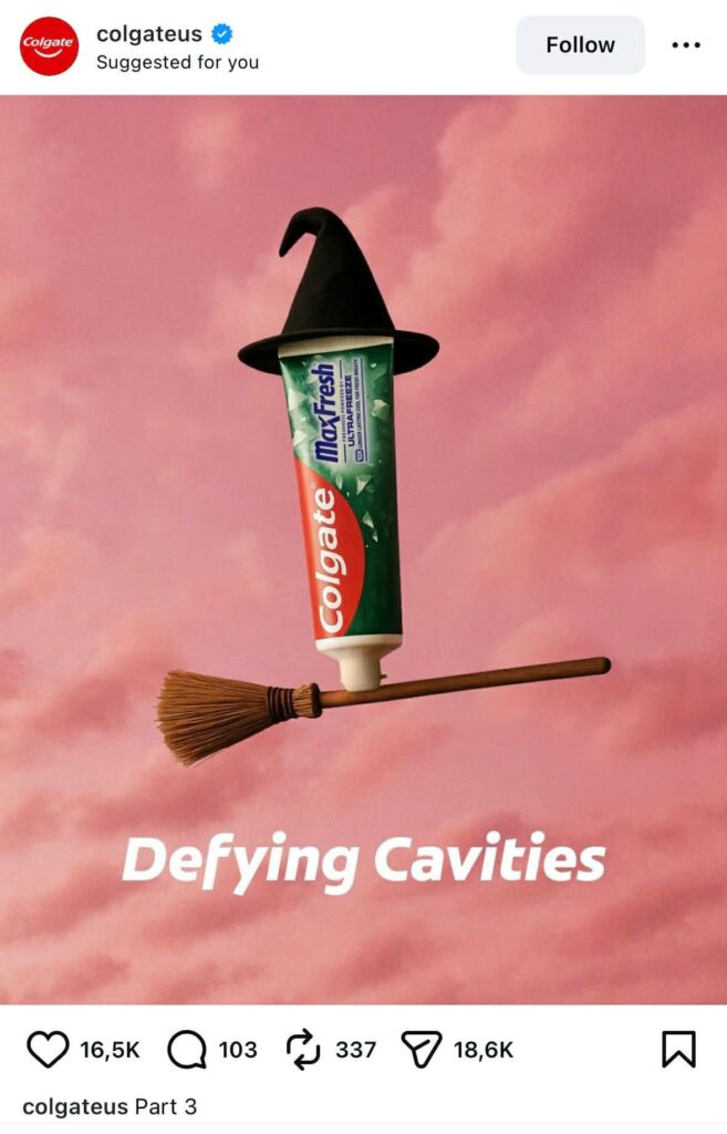 A Colgate MaxFresh toothpaste tube wearing a black witch hat and flying on a broomstick against a pink cloudy background. White text below reads “Defying Cavities.”
