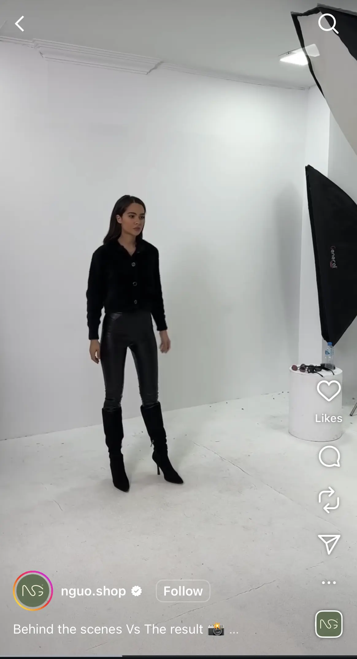 A behind-the-scenes look in a Reel at a fashion shoot shows a model in a black top, shiny black pants, and heeled boots posing in a white studio with professional lighting equipment.