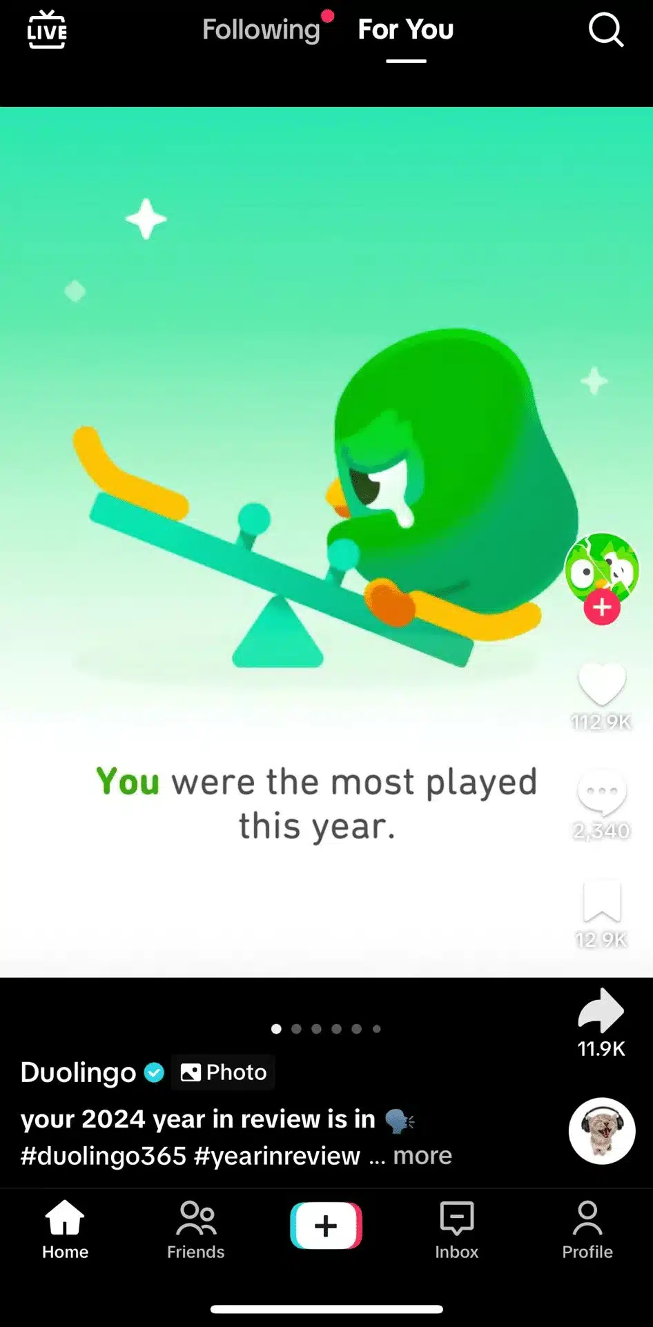 TikTok slideshow post by Duolingo showing a sad green owl character on a seesaw with the caption “You were the most played this year,” indicating a personalized year-in-review moment. TikTok interface elements like likes, comments, and share buttons are visible.