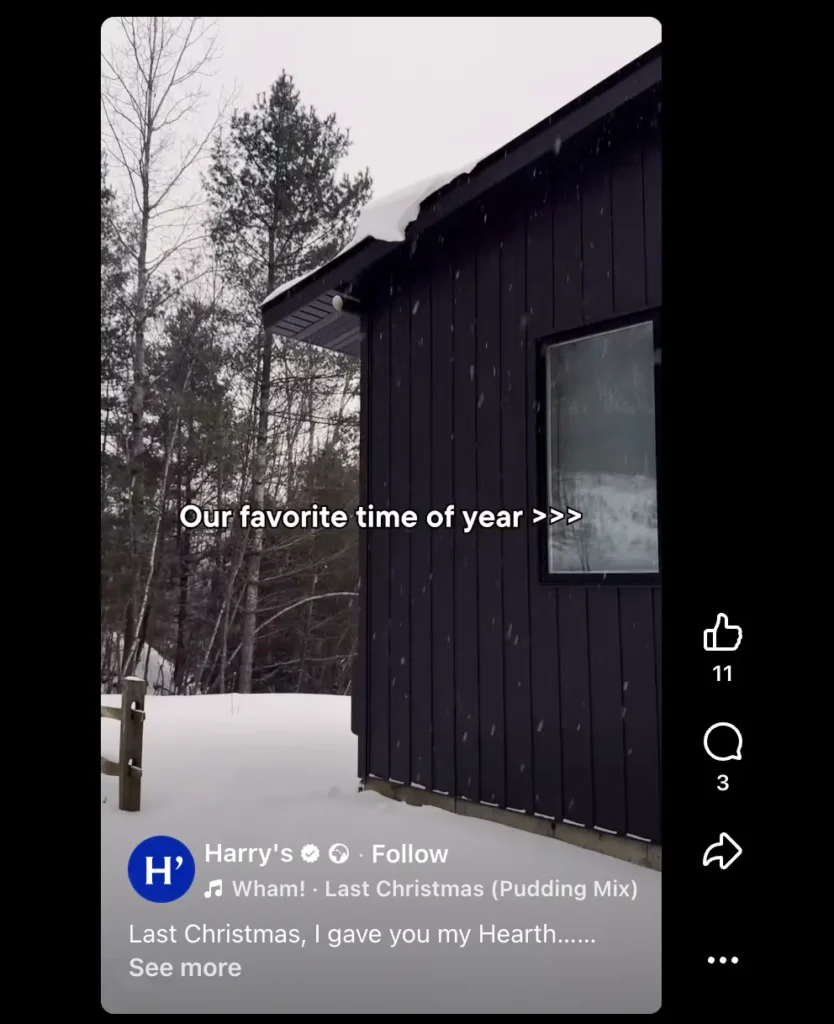 Snow falling beside a dark wooden building surrounded by trees, with text overlay reading “Our favorite time of year.”
