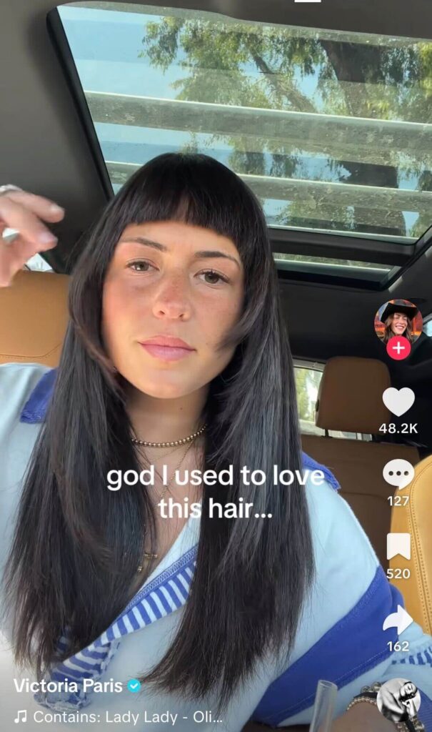A woman sits in her car showing her long dark hair with short bangs, with on-screen text saying “god I used to love this hair…”
