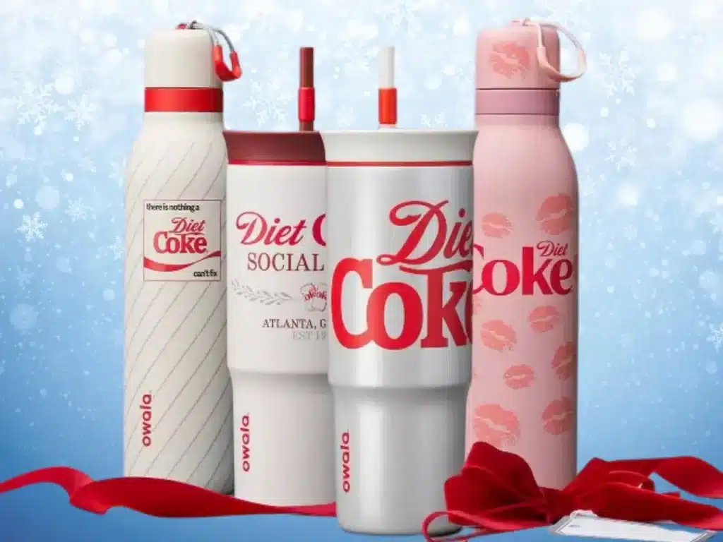 A collection of Coca-Cola–branded Owala reusable water bottles in red, white, and pink, displayed against a festive winter-themed background.