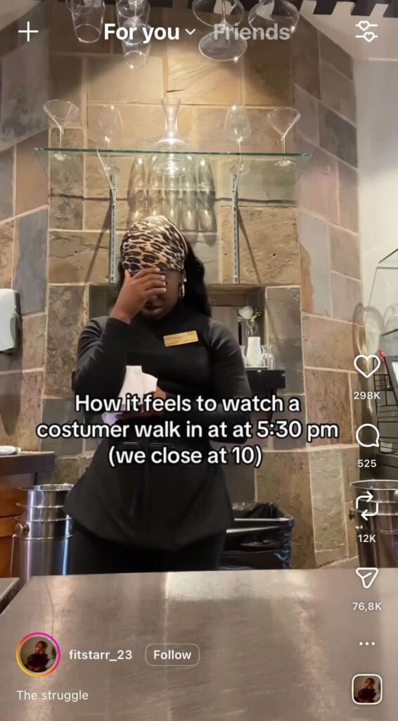 A restaurant worker stands behind a counter, covering their face with one hand in visible frustration. On-screen text reads, “How it feels to watch a customer walk in at 5:30 pm (we close at 10).”