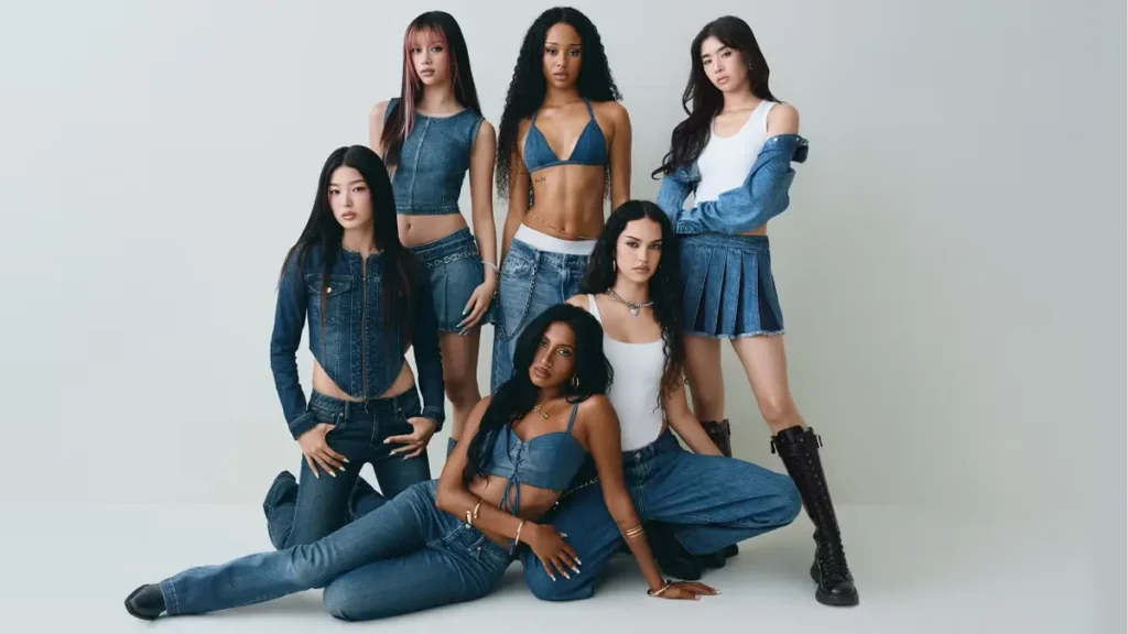 A group of seven women wearing coordinated denim outfits, posed together in a studio setting for a fashion campaign.