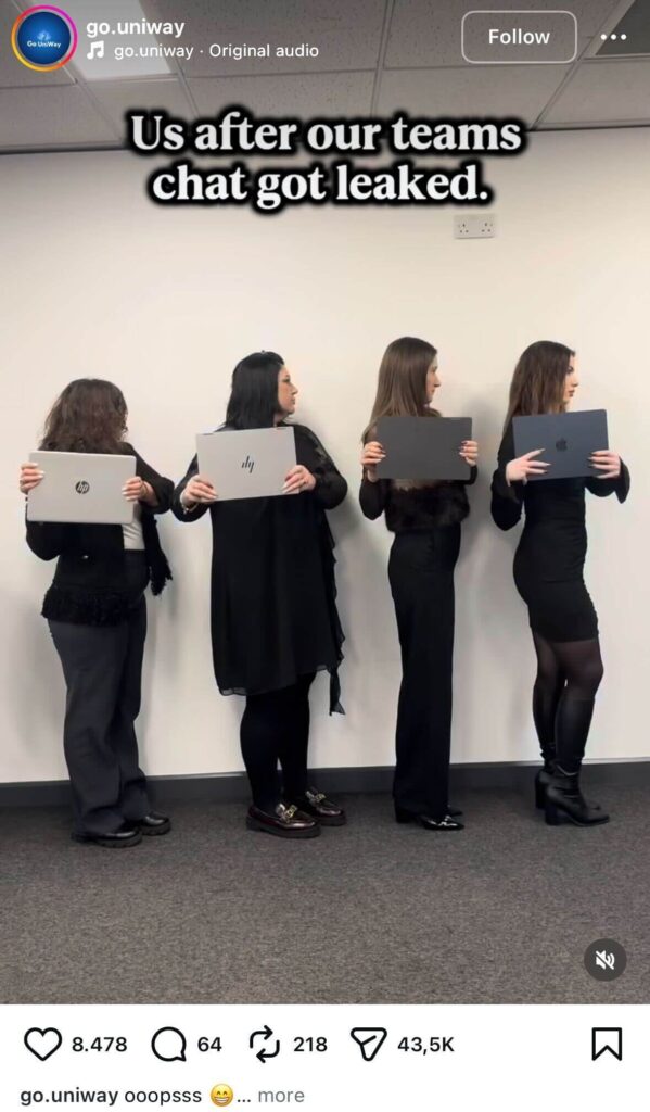 Four women dressed in black stand side by side against a white wall, each holding a closed laptop and looking to the side, with on-screen text reading, “Us after our teams chat got leaked.”