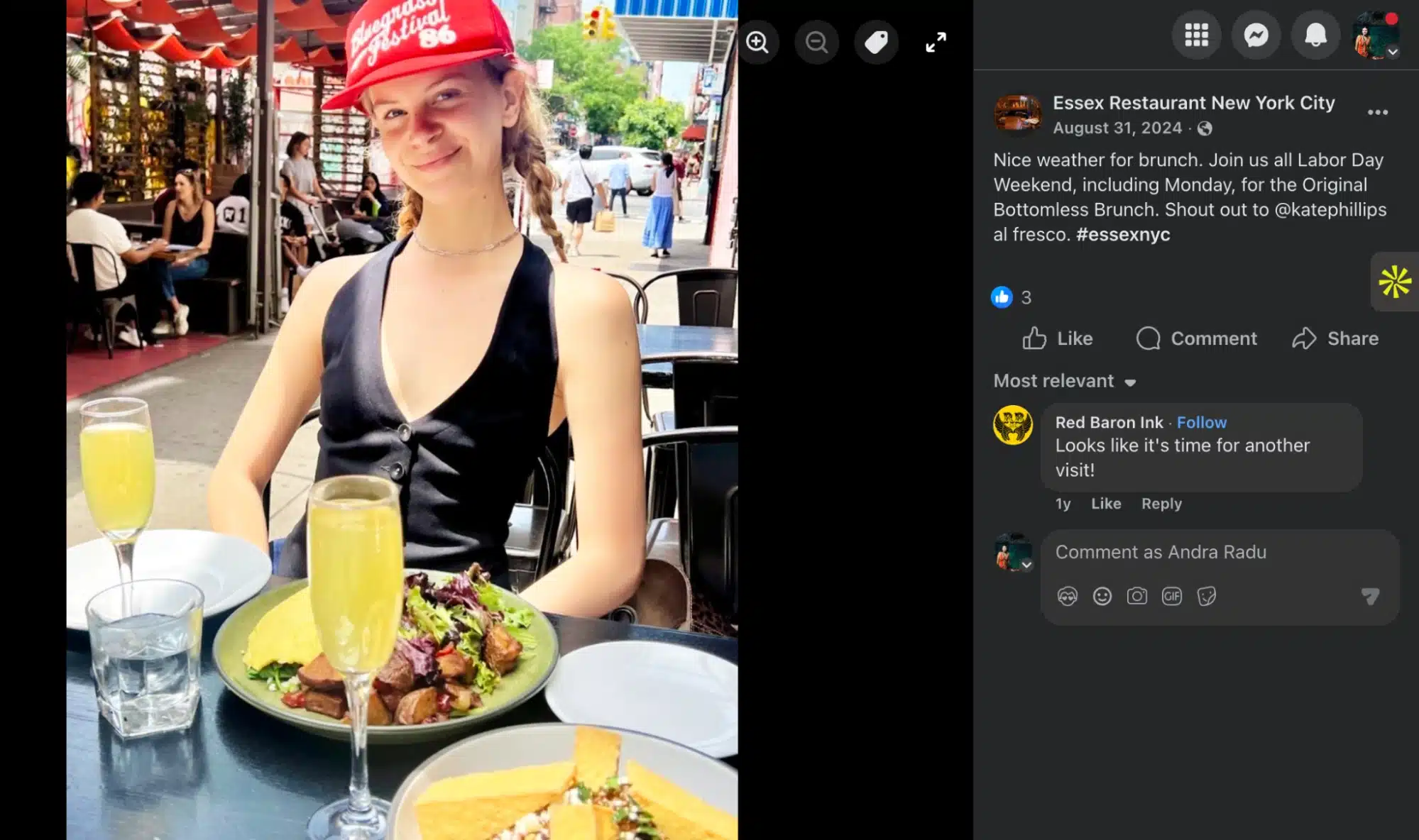 A woman sitting at an outdoor restaurant table with plates of food and two glasses of orange-colored drinks, smiling at the camera.