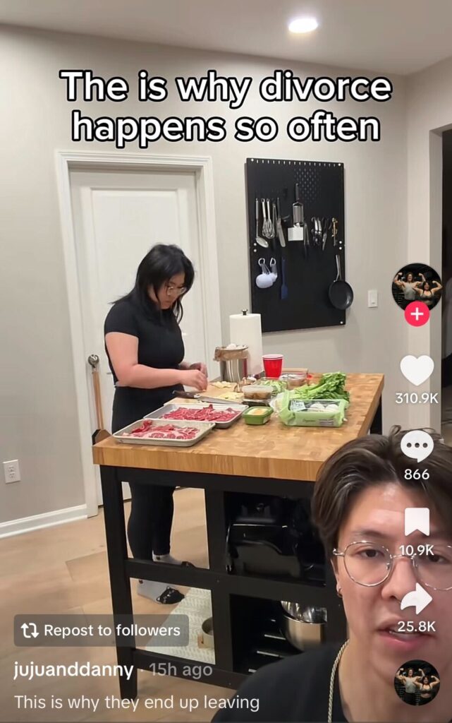 Two people in a kitchen, one preparing food at an island while the other films from the foreground; on-screen text reads, “This is why divorce happens so often.”