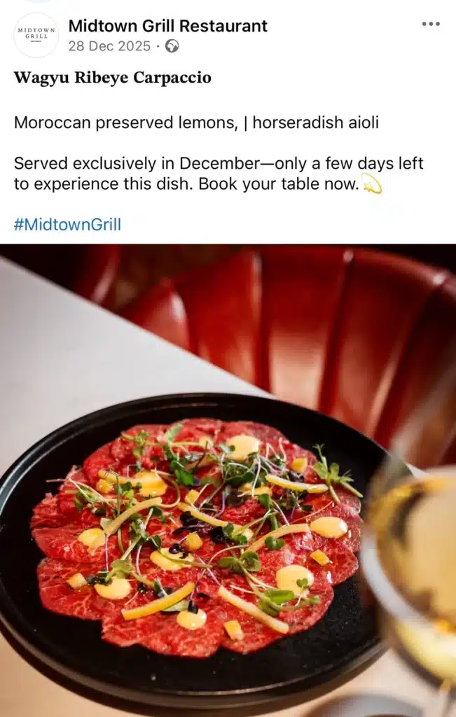 Close-up of a plated Wagyu ribeye carpaccio topped with microgreens, sauce, and preserved lemon, served on a black plate in a restaurant setting