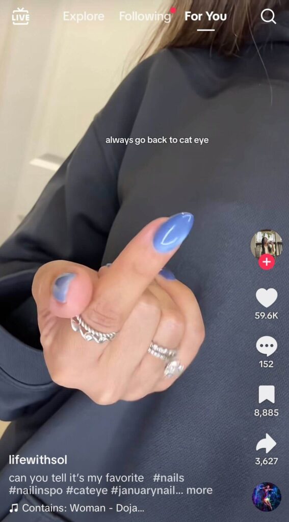 Close-up of a hand with glossy blue cat-eye nails and silver rings, held against a dark hoodie. On-screen text reads, “always go back to cat eye.”