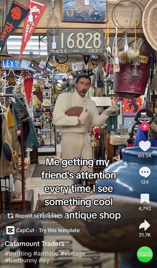 Screenshot from a TikTok video showing Bad Bunny inside a crowded antique shop filled with vintage signs, license plates, and decor. On-screen text reads, “Me getting my friend’s attention every time I see something cool at the antique shop,” with TikTok engagement icons on the right.