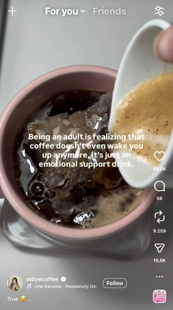 Close-up of iced coffee in a pink mug as espresso is poured over ice. On-screen text reads, “Being an adult is realizing that coffee doesn’t even wake you up anymore, it’s just an emotional support drink.”