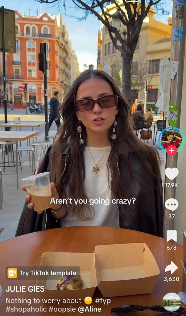 Woman sitting at an outdoor café holding an iced coffee with text overlay “Aren’t you going crazy?” in a TikTok-style video format.
