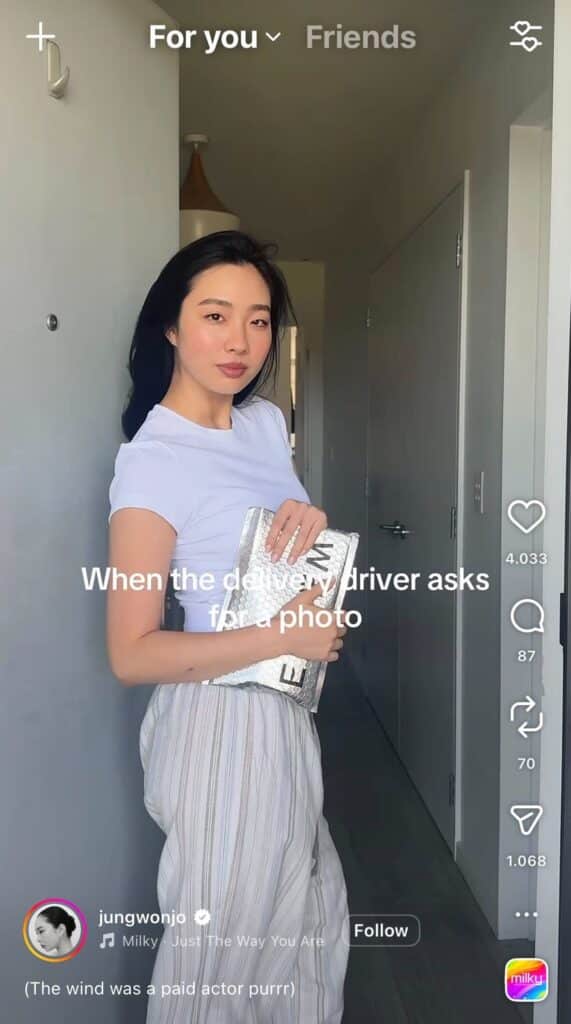 Woman holding a package posing in a hallway with text overlay “When the delivery driver asks for a photo” in an Instagram Reel