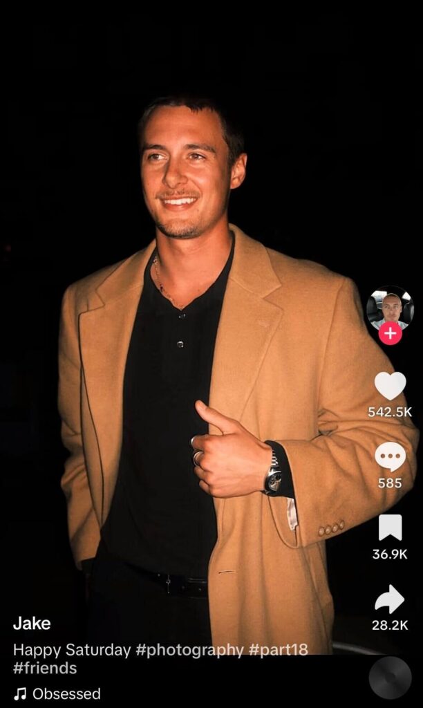 Man wearing a camel coat and black shirt posing at night, shown in a TikTok post with caption and engagement icons on screen.