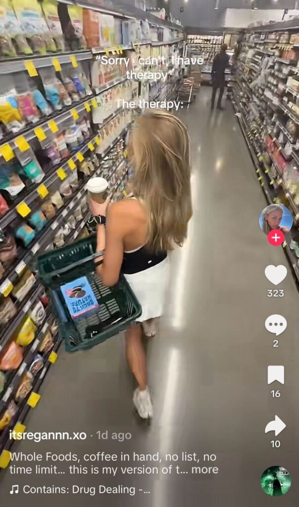 Woman walking through a grocery store aisle holding a coffee and basket with text overlay about “therapy,” shown in a TikTok video interface with engagement icons.