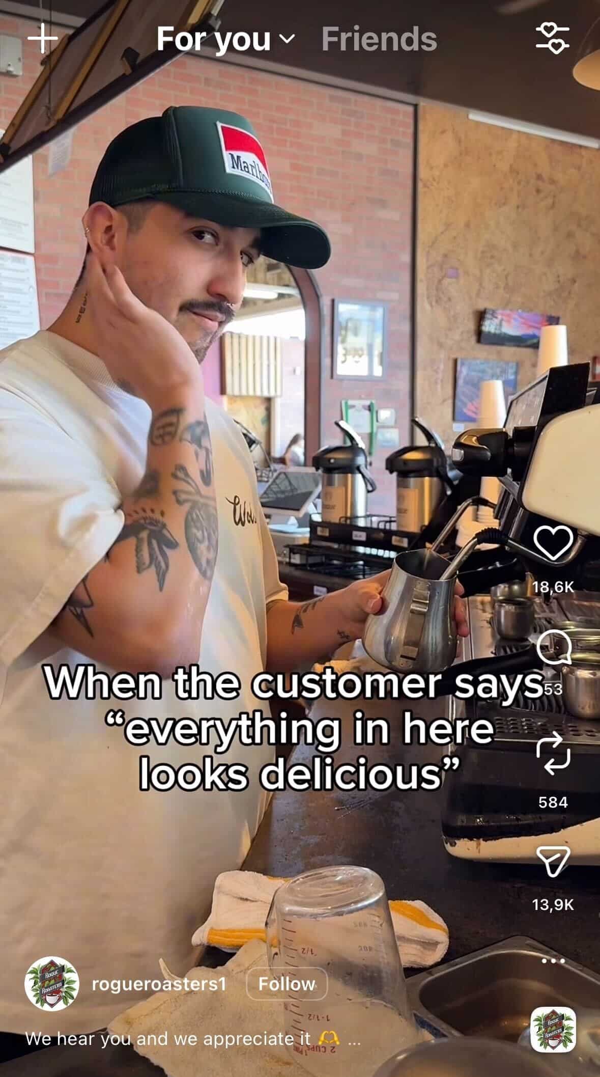 Barista with tattoos and a cap stands behind a coffee machine holding a milk pitcher, with text overlay joking about customers saying everything looks delicious.