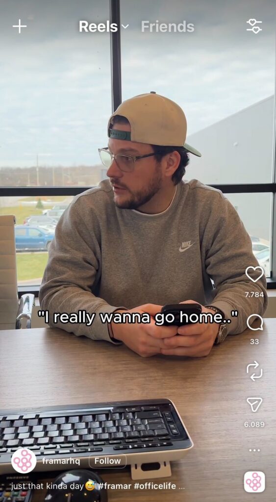 Man wearing glasses and a backwards cap sits at a desk holding his phone, looking tired in an office setting with text overlay saying “I really wanna go home.”