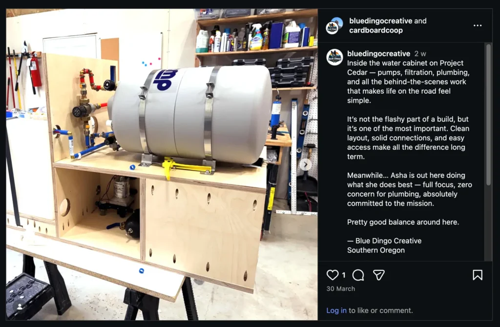 Large water tank and plumbing system installed on a wooden cabinet in a workshop, with tools and supplies in the background.