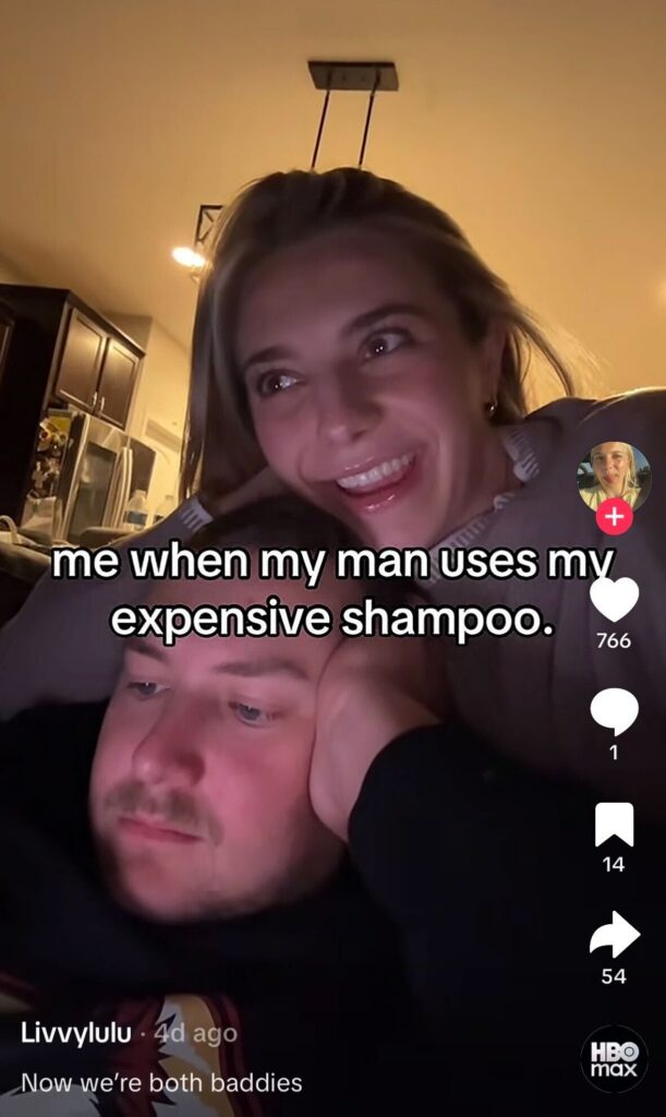 A couple sitting together at home, with the woman smiling mischievously while text jokes about her reaction when her partner uses her expensive shampoo.