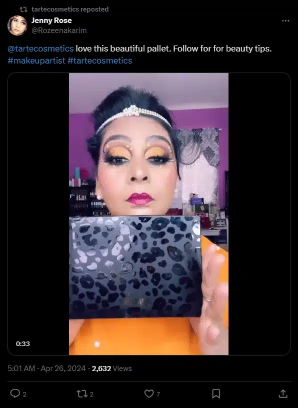 Tweet repost featuring a beauty creator holding a black leopard-print makeup palette close to the camera. The creator wears bold, colorful eye makeup with glitter and a headband, posing in a room with pink walls and beauty products in the background.