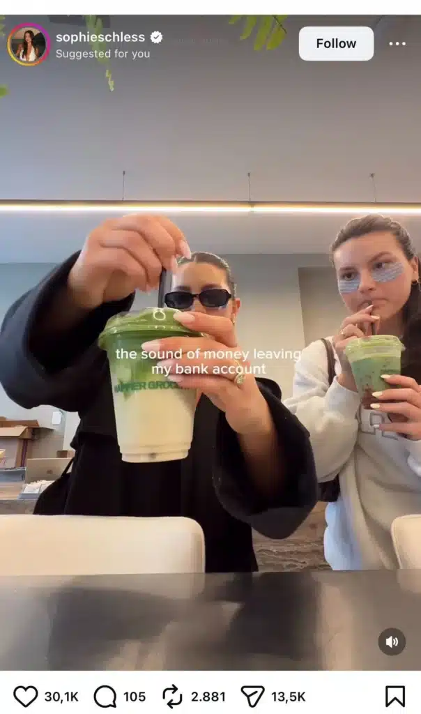 : Two women stir iced matcha drinks while text jokes about “the sound of money leaving my bank account” in a relatable spending trend video.