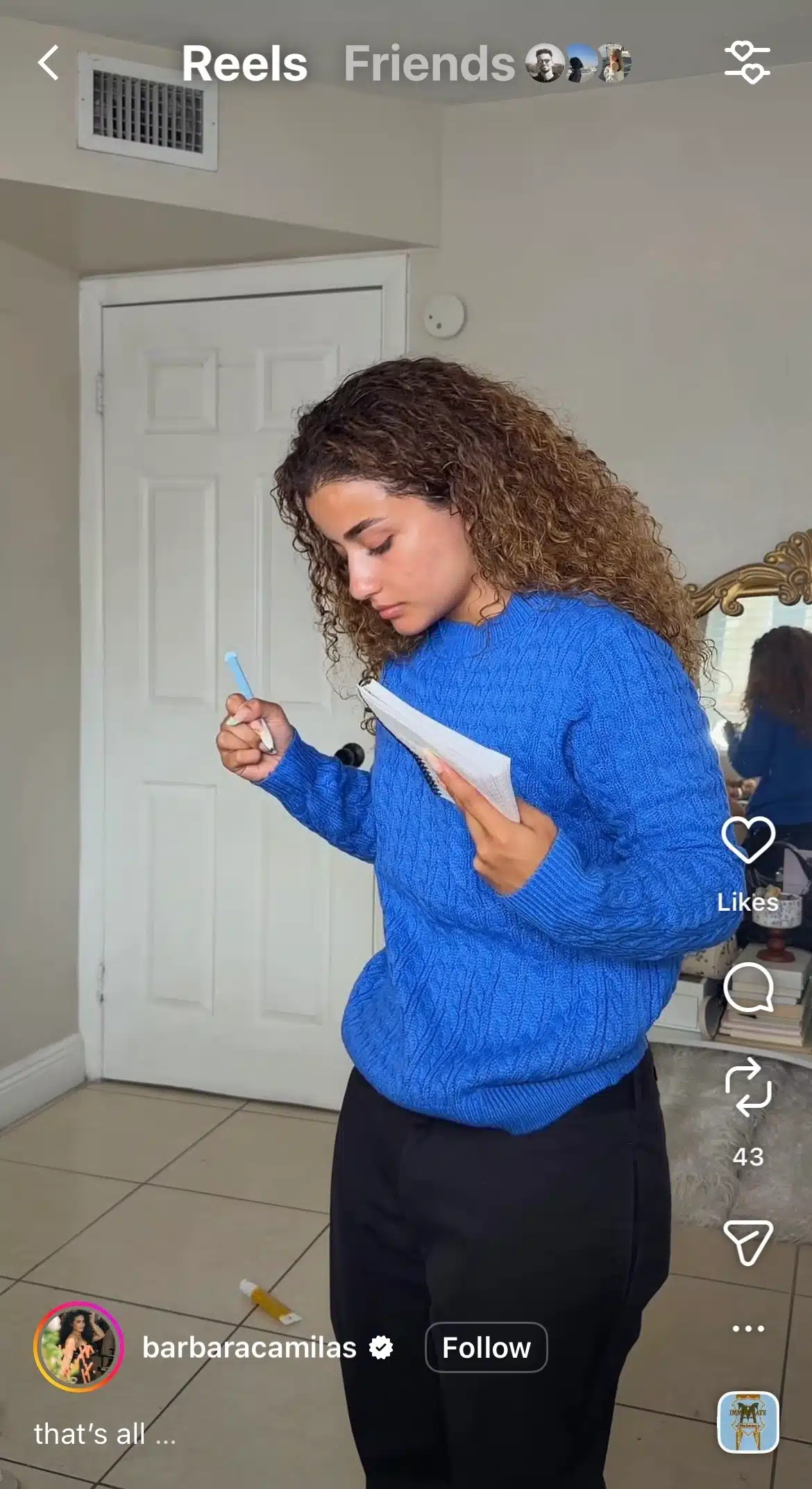 Instagram Reel showing a woman in a blue sweater holding a pen and notebook while standing in a bedroom, with Instagram Reels interface elements visible on screen.