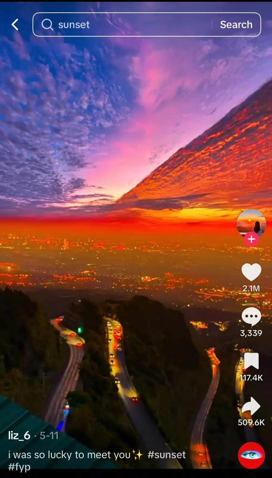 TikTok video showing a dramatic purple and orange sunset over a city and winding mountain roads, with the word “sunset” in the search bar and glowing city lights below the sky.