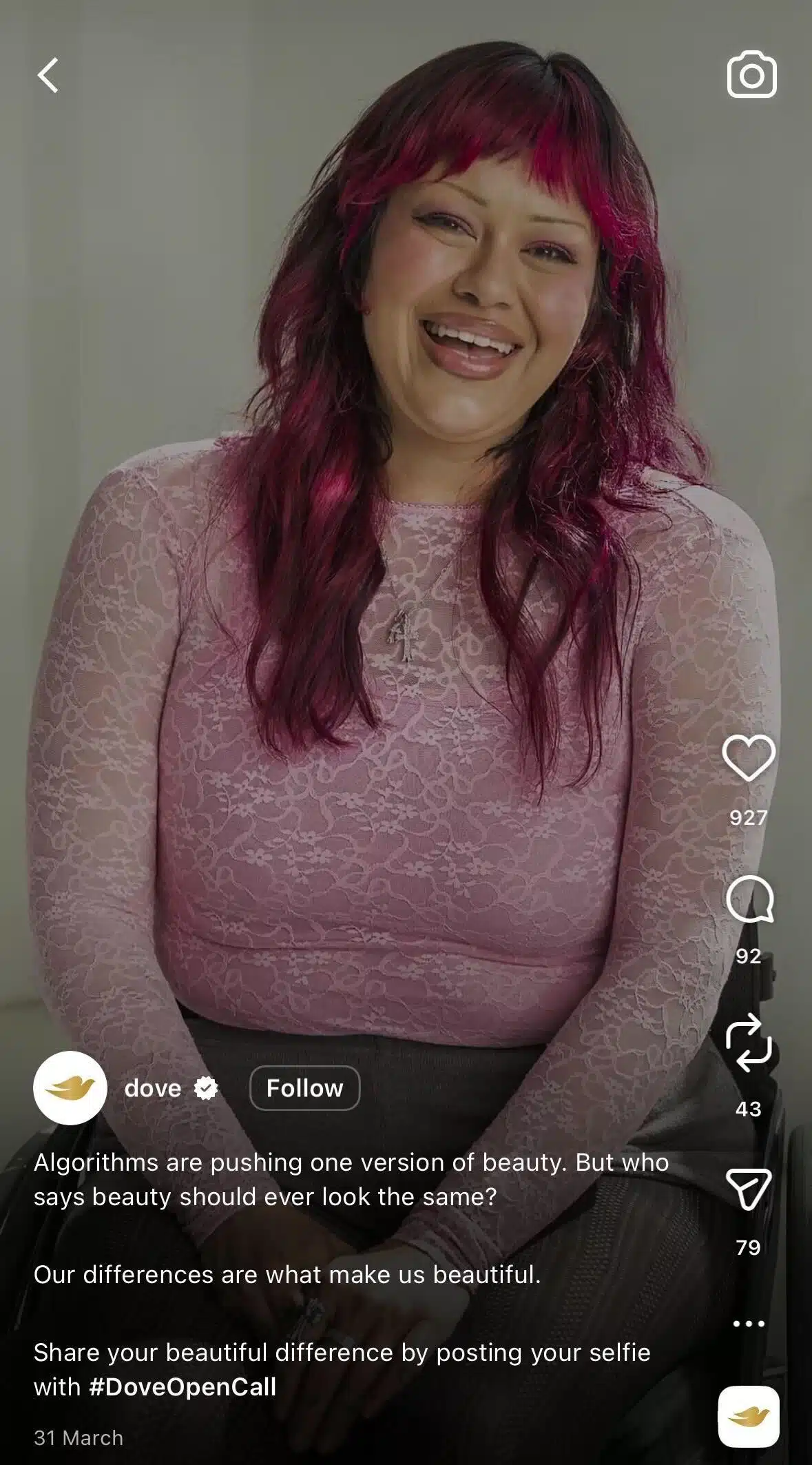 A smiling woman with shoulder-length dark magenta hair and bangs sits facing the camera against a light background. She wears a fitted long-sleeve pink lace top and a necklace with a cross pendant. White text in the caption area discusses beauty standards and the hashtag #DoveOpenCall. TikTok interface elements appear along the right side.