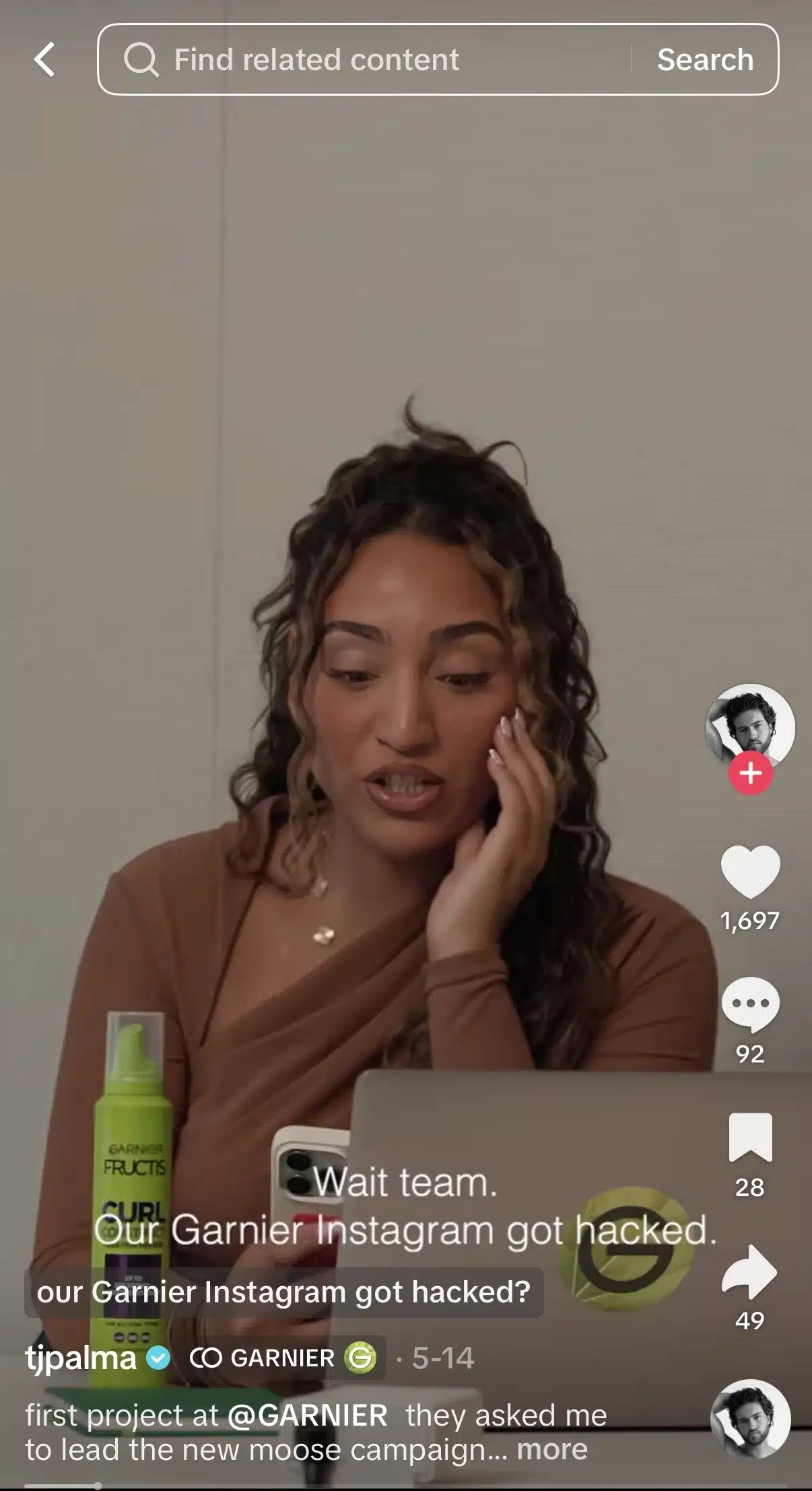 A woman with long curly hair sits at a desk looking at a smartphone and laptop. A green bottle of Garnier Fructis Curl product stands on the desk beside her. White overlay text reads, “Wait team. Our Garnier Instagram got hacked.” TikTok interface elements and engagement icons are visible.
