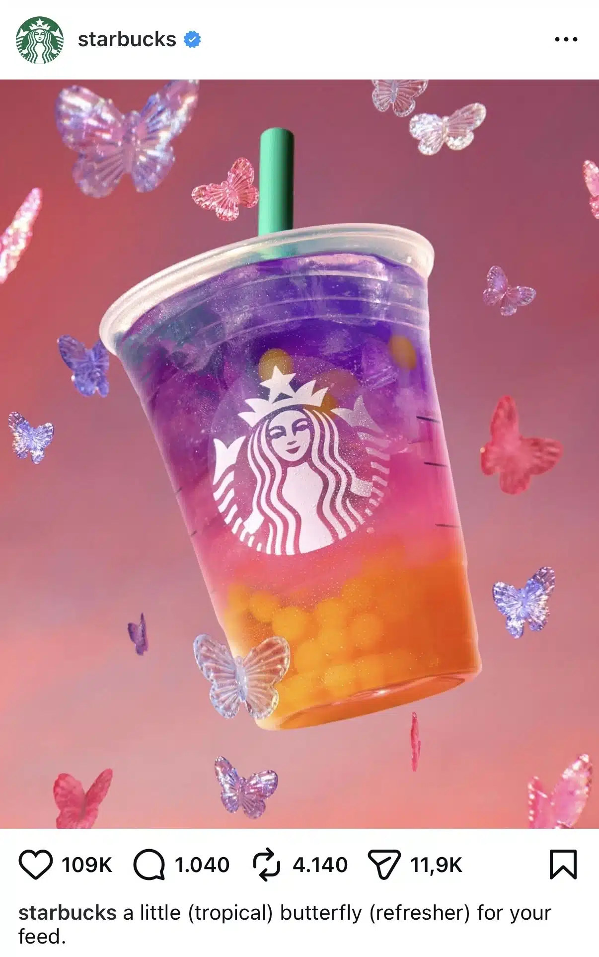 A Starbucks cold drink floats against a pink and purple gradient background. The beverage contains layers of orange, pink, and purple liquid with ice cubes visible inside a clear plastic cup featuring the Starbucks logo. Decorative translucent butterflies in pink, purple, and blue surround the drink. Instagram interface elements and the Starbucks account header are visible.