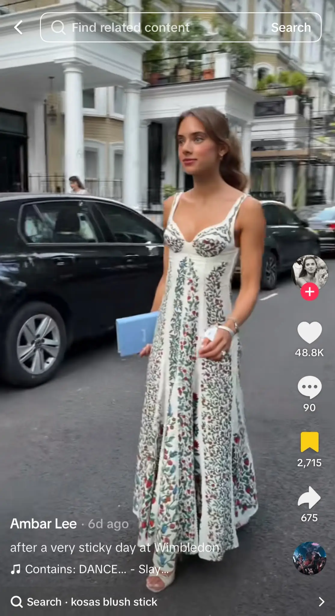 Instagram Reel showing a creator walking down a residential street in a floral maxi dress while holding a blue item, remaining perfectly still as the camera moves around them. The Reel demonstrates the revived Mannequin Challenge trend, where people freeze in place while the camera continues moving.