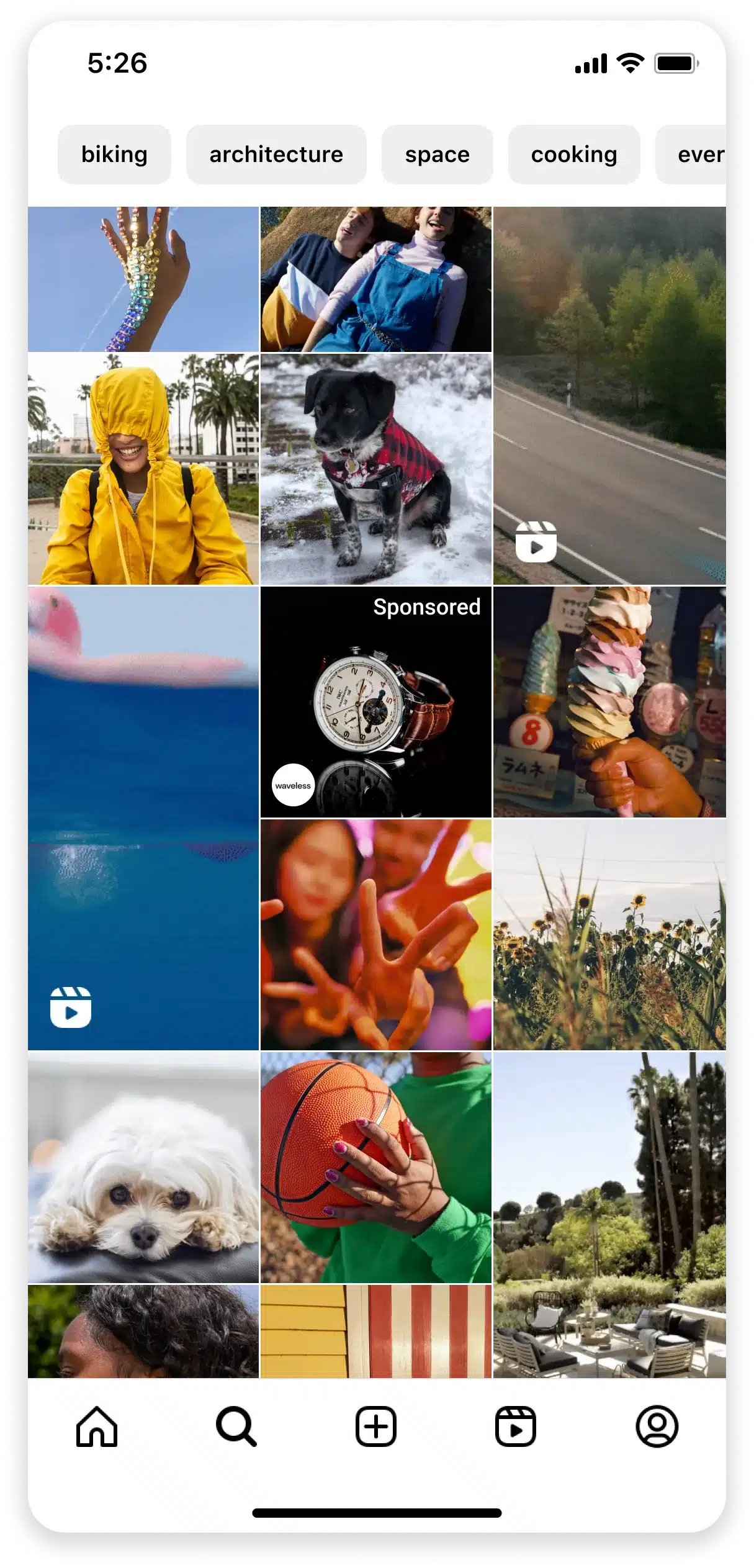 Instagram Explore page displaying a grid of recommended photos and Reels organized under interest categories such as biking, architecture, space, and cooking. The feed includes a mix of lifestyle, pets, landscapes, food, and people, with a Sponsored watch advertisement appearing among the recommended content and Reel icons marking video posts. The bottom navigation bar highlights the Search/Explore tab.